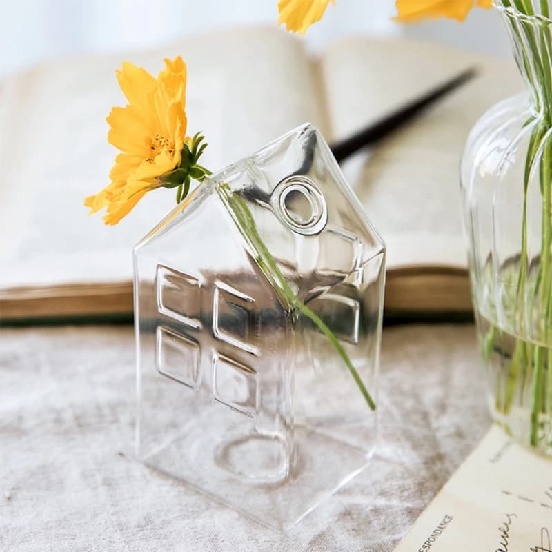 Vaso de vidro transparente em formato de casa com flor amarela para decoração de mesa