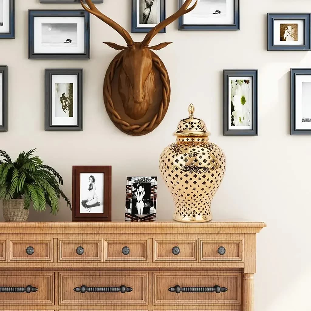 Vaso decorativo dourado em cerâmica com tampa, design vazado geométrico, sobre móvel de madeira