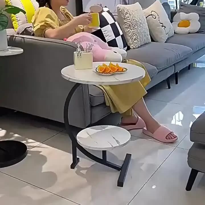Mesa lateral minimalista branca com tampo redondo em mármore e base preta ao lado de sofá cinza