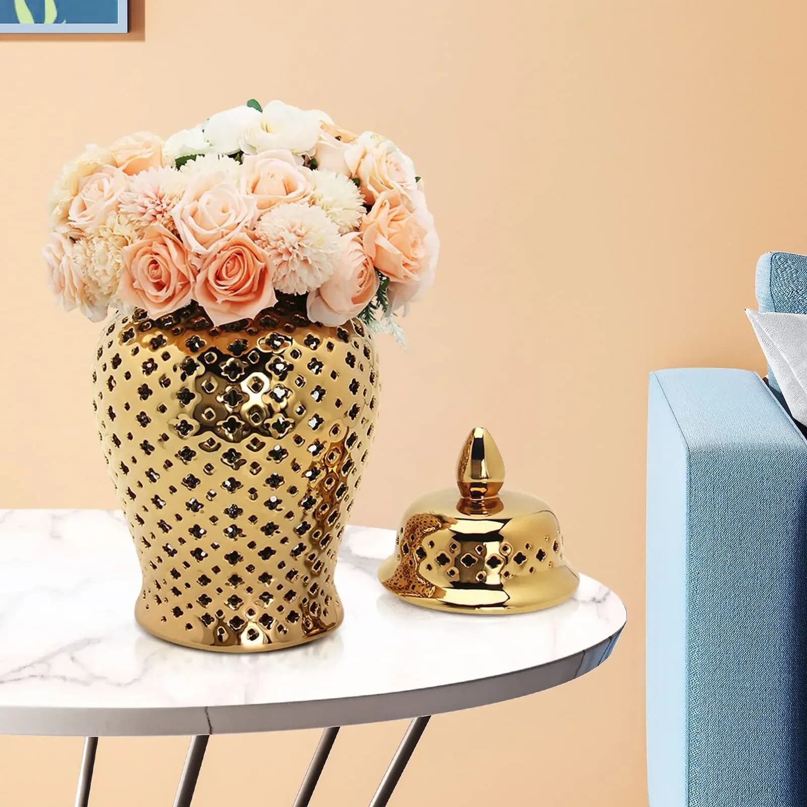 Vaso decorativo dourado em cerâmica com design vazado geométrico e flores em mesa branca