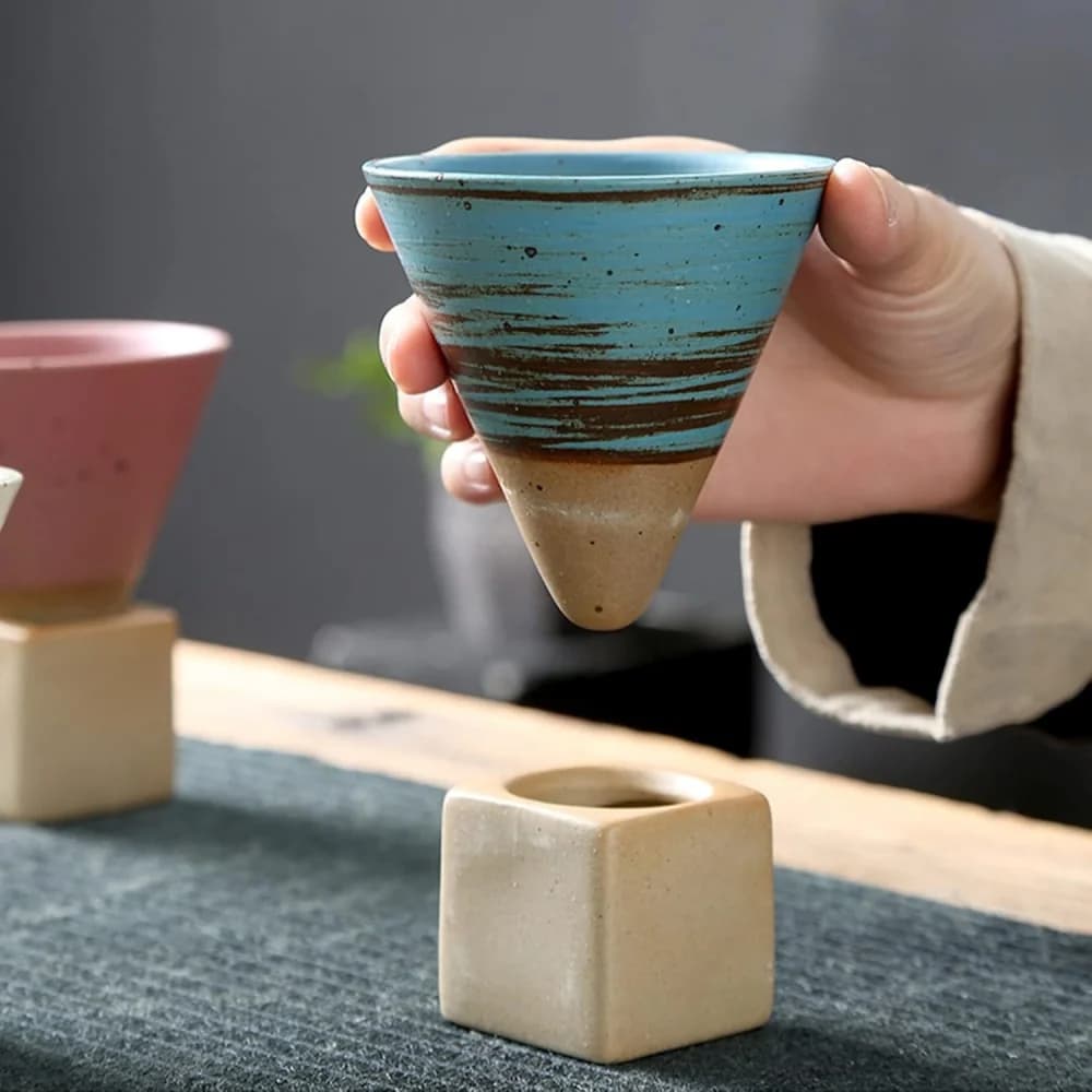 Caneca de café azul com detalhes marrons segurada à mão com base quadrada bege estilo japonês