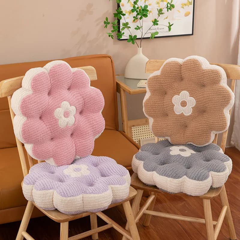 Sete almofadas decorativas de pelúcia em forma de flor, cores pastel, sobre um sofá marrom