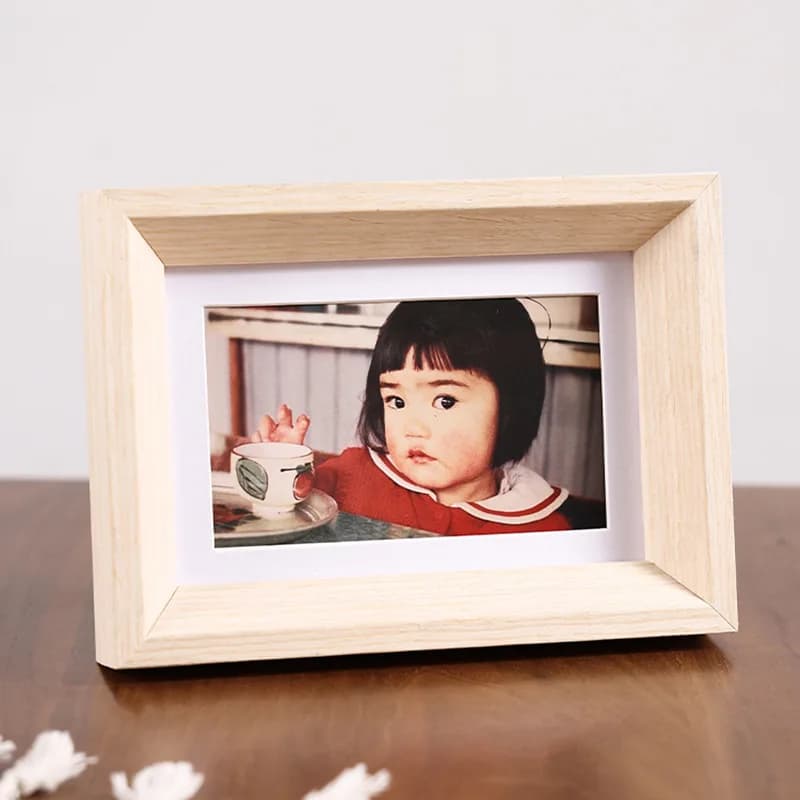 Porta-retratos minimalistas em madeira e branco em uma mesa de madeira com um tecido de crochê branco.