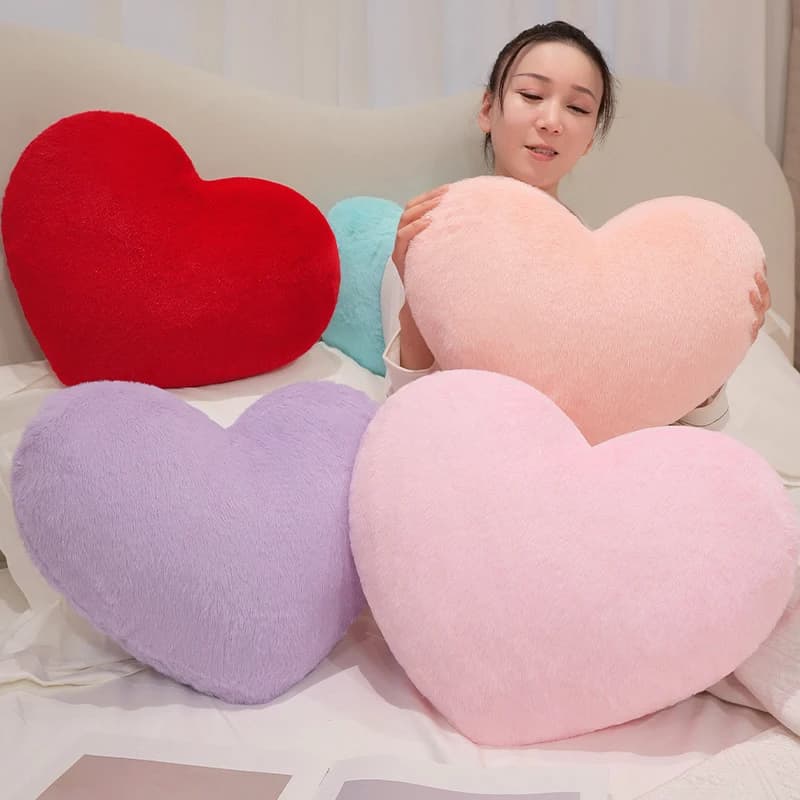 Mulher segurando almofada peluda pêssego em formato de coração com almofadas vermelha, lilás, rosa e azul claro ao redor