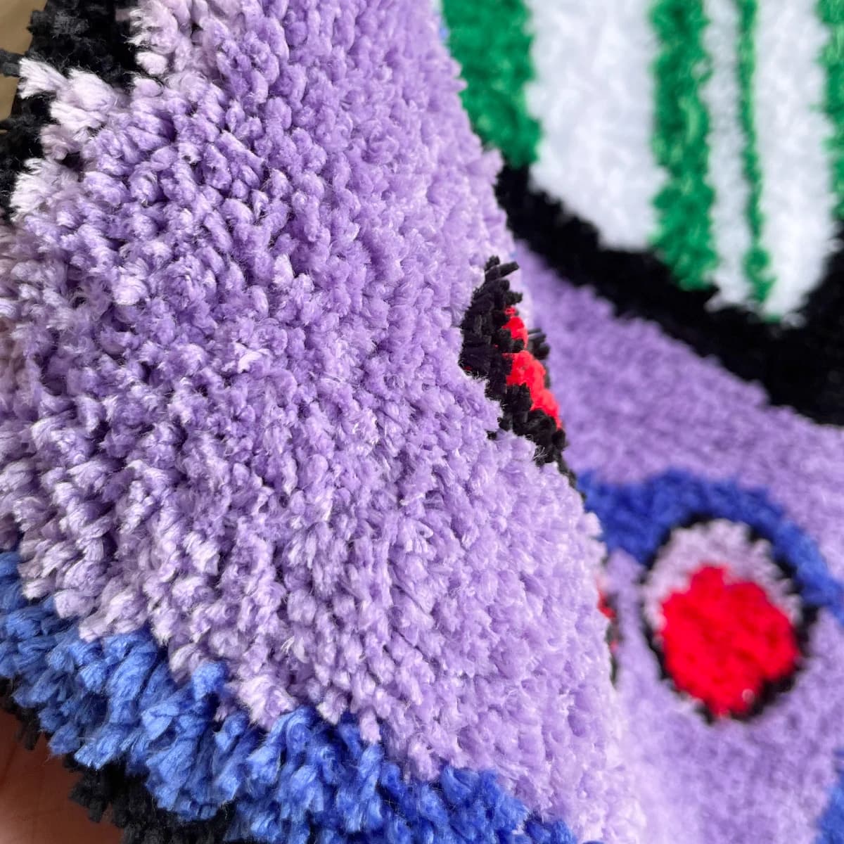 Detalhe em close do material tufado e cores vibrantes do tapete gamer console roxo