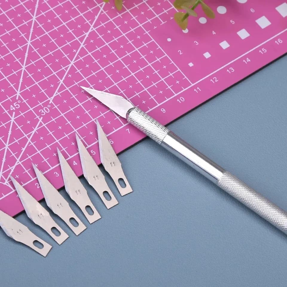 Kit 5 lâminas de reposição para cortador de gravura profissional com cabo prata sobre mesa azul