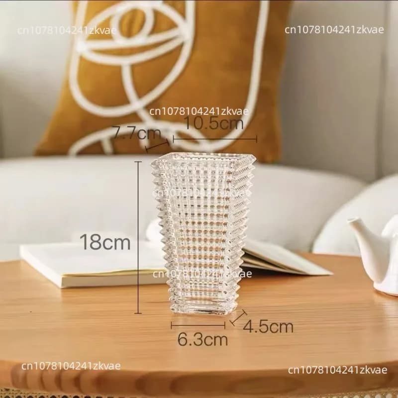 Vaso de vidro transparente com design geométrico sobre mesa de madeira, ao lado de chaleira e livro.