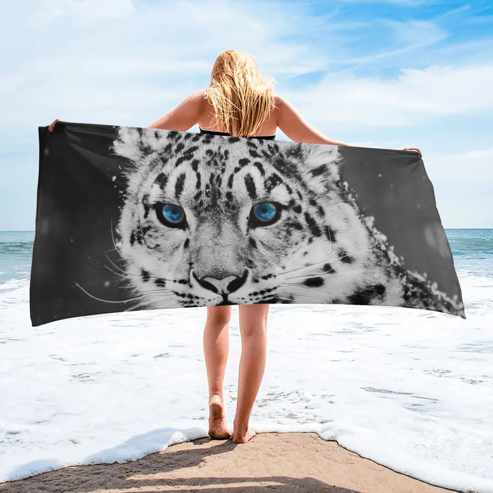 Toalha de praia com tigre e filhotes em fundo nevado, segura por uma mulher na praia.