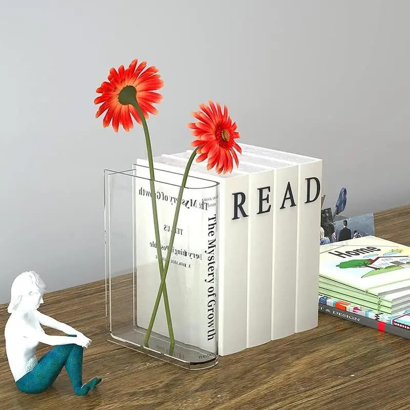 Vaso acrílico transparente formato livro com flores vermelhas em mesa de madeira ao lado de decoração