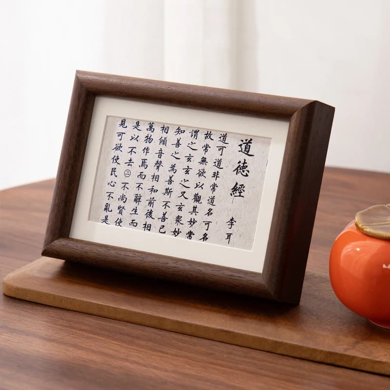 Quadro decorativo de madeira com texto preto sobre fundo branco, mesa de madeira, urna laranja com tampa dourada