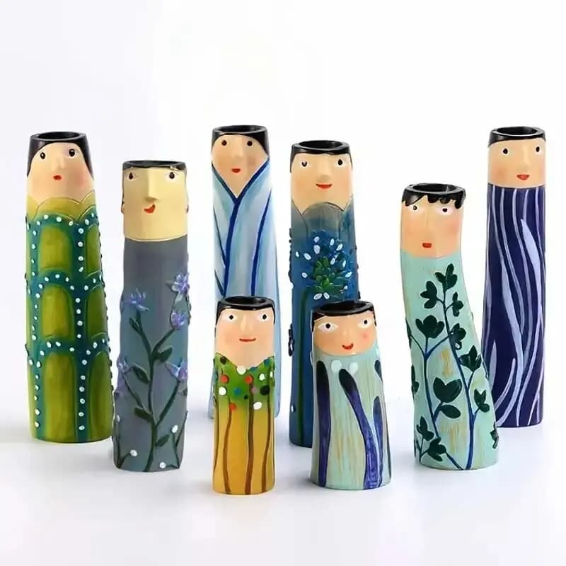 Sete vasos de cerâmica familiares pintados à mão, com rostos e detalhes florais, dispostos em uma linha contra um fundo branco.