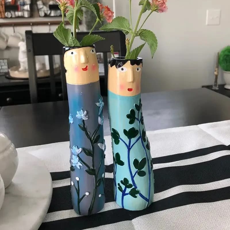 Sete vasos de cerâmica familiares pintados à mão, com rostos e detalhes florais, dispostos em uma linha contra um fundo branco.