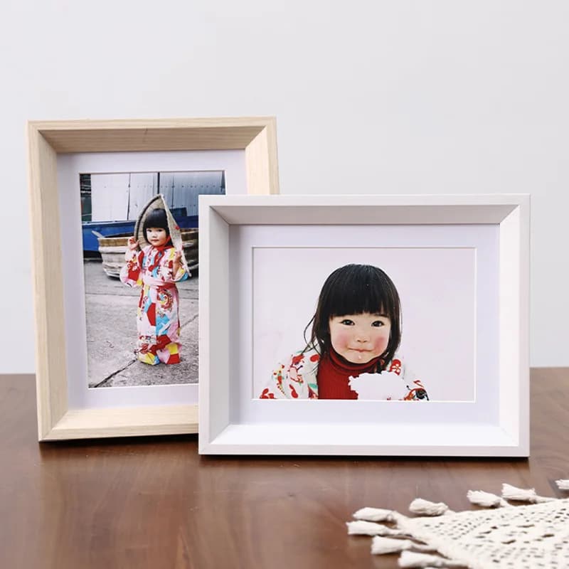 Porta-retratos minimalistas em madeira e branco em uma mesa de madeira com um tecido de crochê branco.
