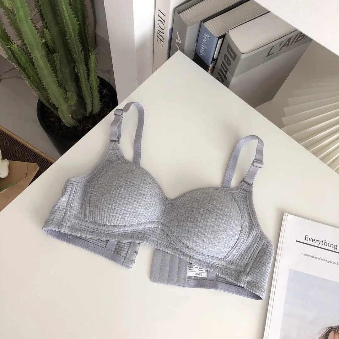 Conjunto de sutiãs sem fio minimalistas em cores sólidas, rosa, preto, cinza e verde claro, dispostos em uma superfície de mármore branco.