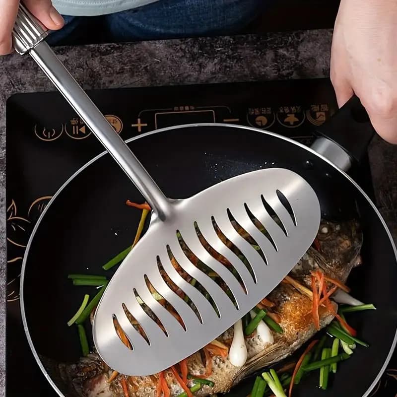 Espátula de cozinha grande em aço inoxidável usada para virar peixe frito em frigideira antiaderente preta