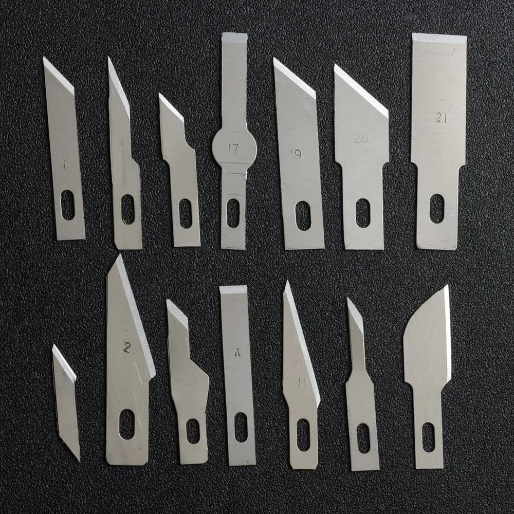Conjunto de 10 lâminas de facas de escultura em metal, com números de identificação e furos para fixação, sobre fundo preto.