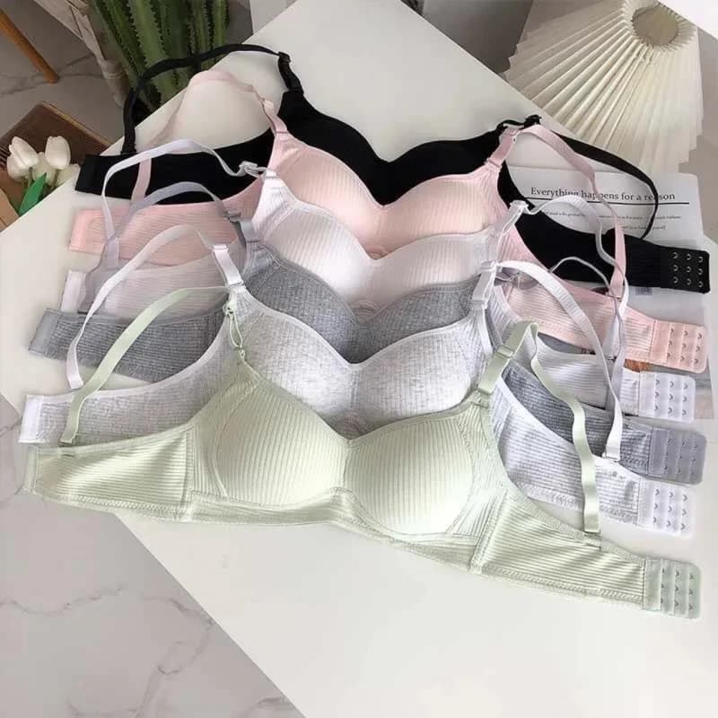 Sutiãs sem fio minimalistas em cores sólidas, rosa, preto, cinza e verde claro, dispostos em uma superfície de mármore branco.