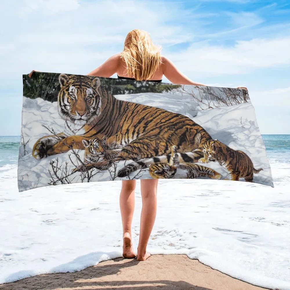 Toalha de praia com tigre e filhotes em fundo nevado, segura por uma mulher na praia.