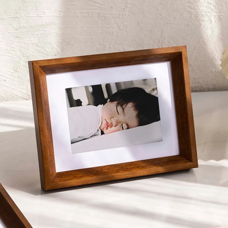 Porta-retrato minimalista em madeira marrom com foto de bebê dormindo em fundo branco