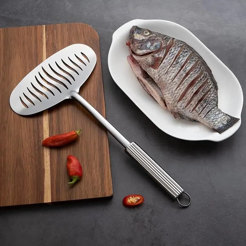Espátula de cozinha grande em aço inoxidável prata com design antiaderente ao lado de peixe cru e pimenta