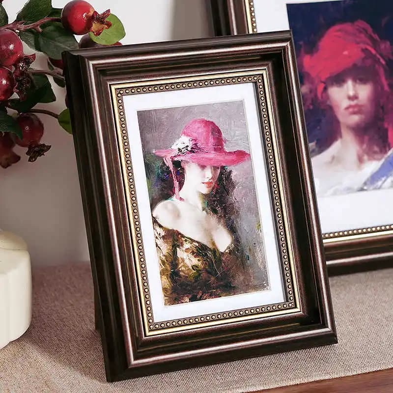 Quadro decorativo americano com moldura de madeira escura e borda dourada, mulher de chapéu rosa