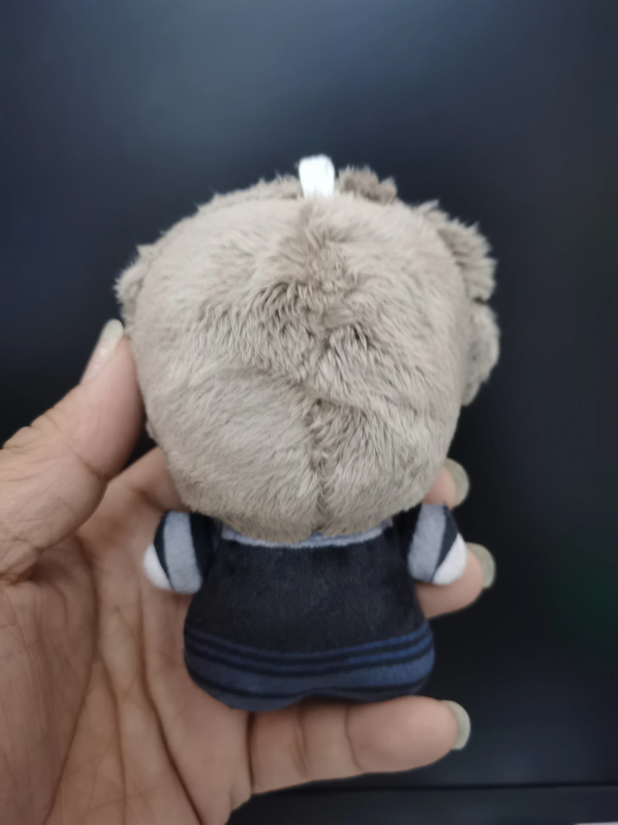 Vista traseira da boneca de pelúcia Gachiakuta Zanka bege com roupa cinza escuro e detalhes em azul 10cm