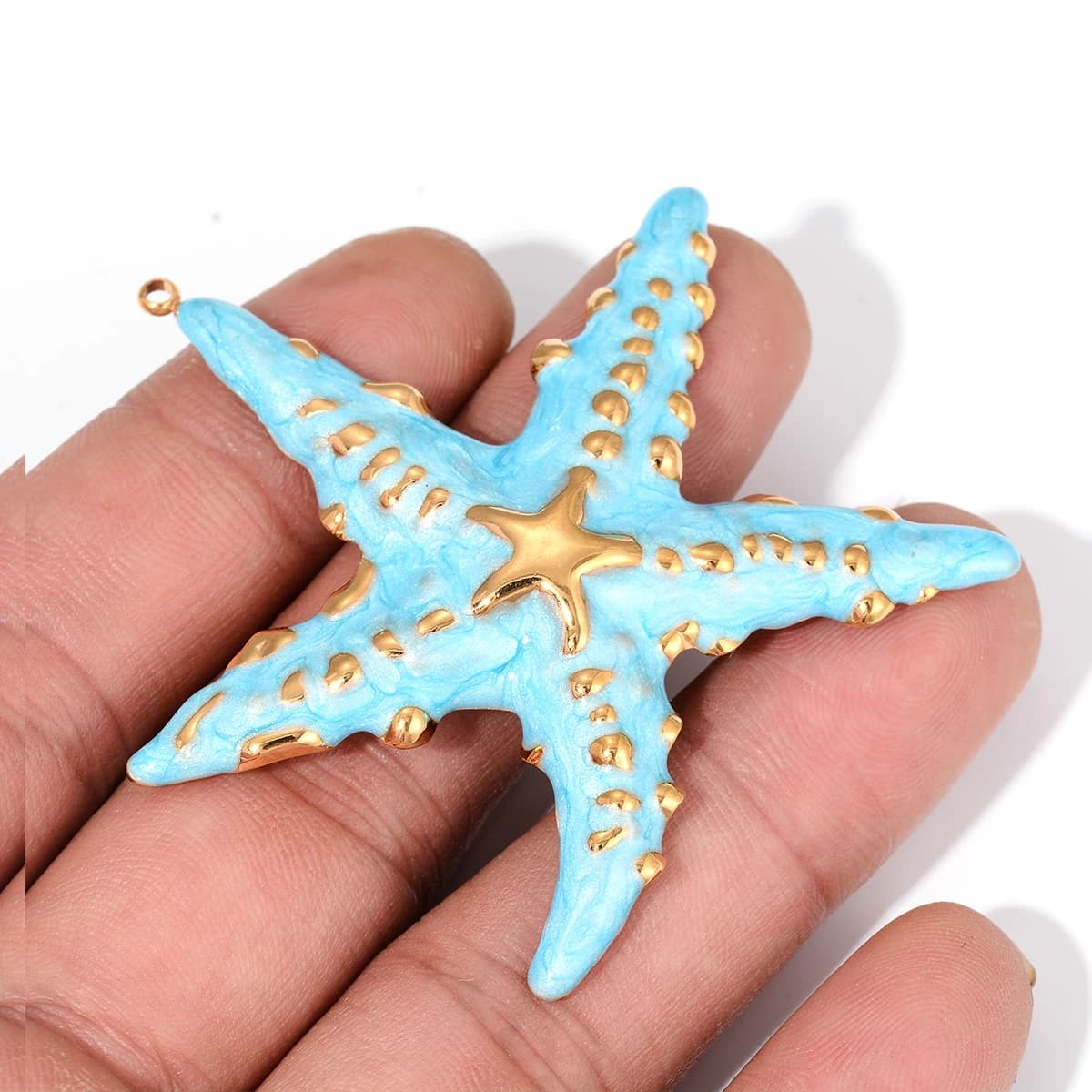 Pingente estrela do mar azul esmaltado com detalhes dourados segurado na mão para escala