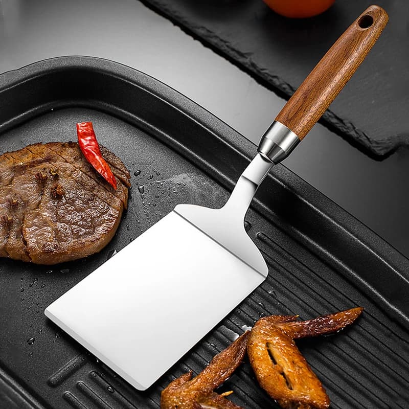 Espátula de bife de aço inoxidável com cabo de madeira em um fundo escuro