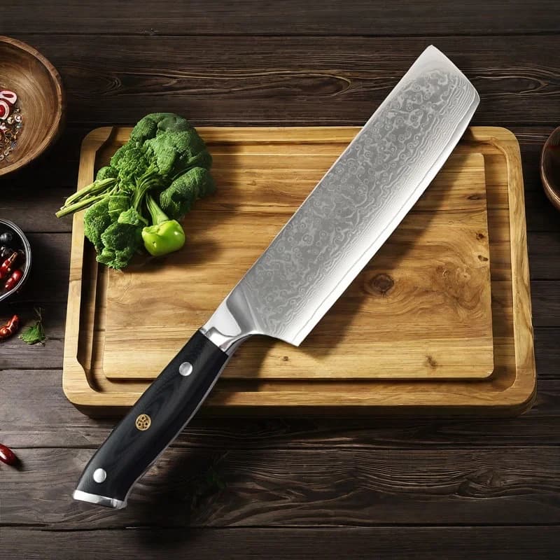 Faca de chef japonesa de 7 polegadas com lâmina damasco e cabo preto sobre tábua de corte com vegetais
