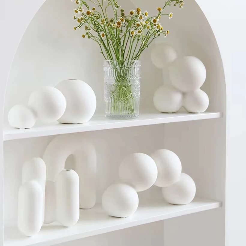 Vasos decorativos Jácotei nórdicos em porcelana branca exibidos em prateleiras brancas com flores artificiais