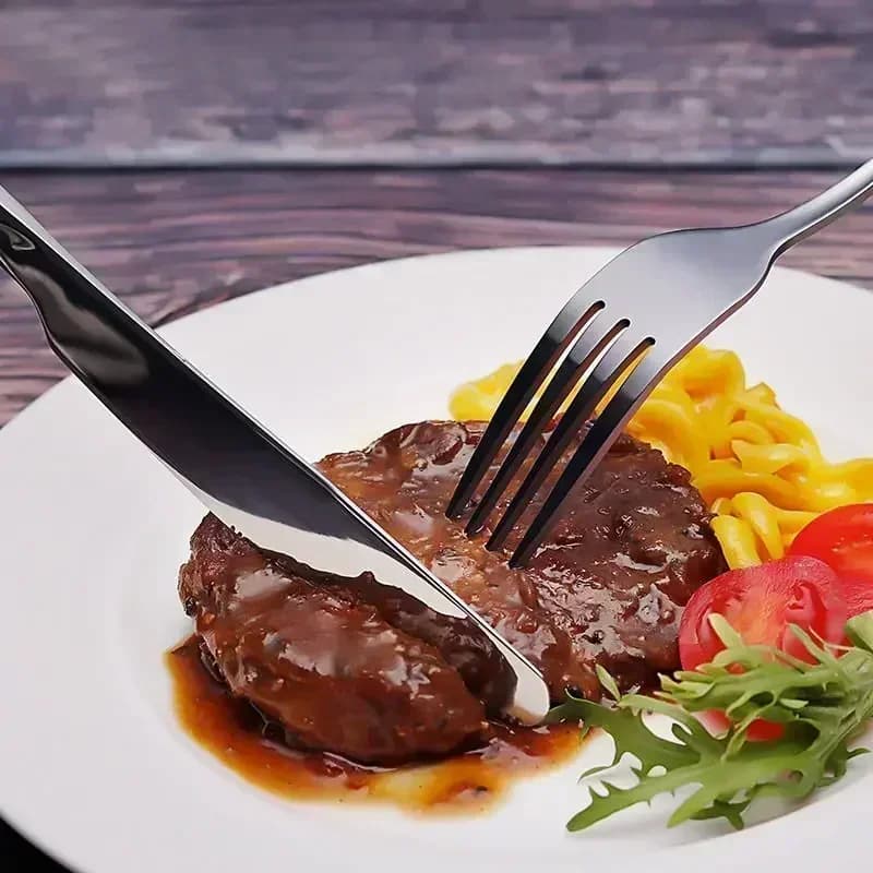 Faca e garfo em aço inoxidável cortando carne em prato branco com macarrão e salada