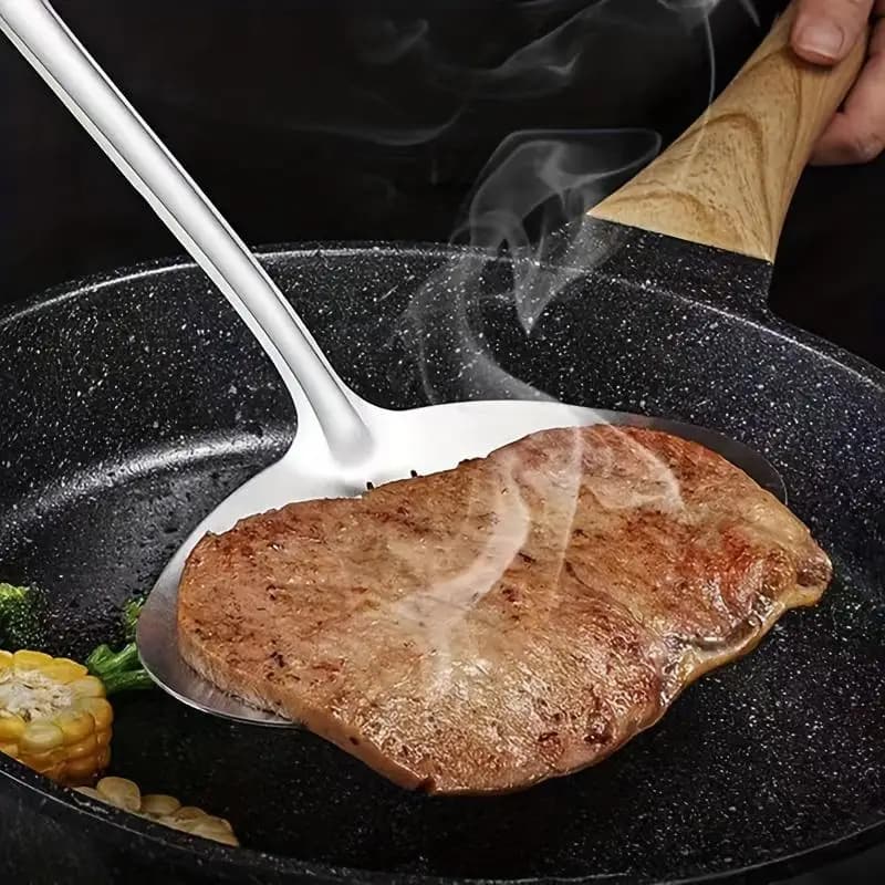 Espátula de cozinha grande em aço inoxidável levantando bife grelhado em frigideira preta com legumes