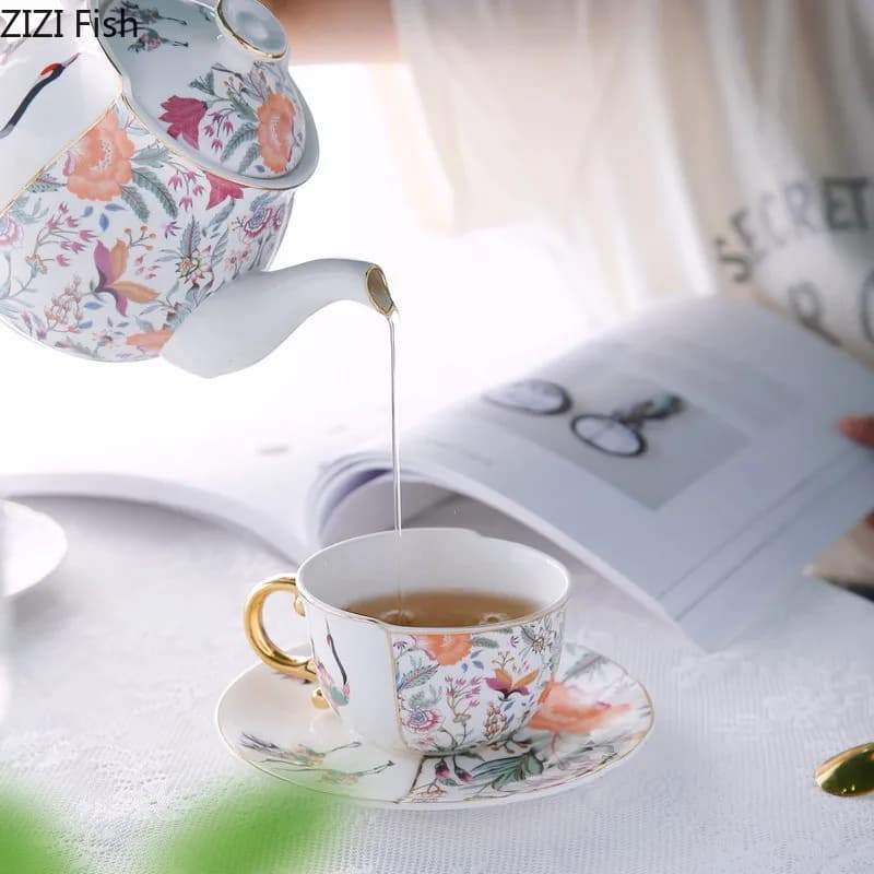 Bule de porcelana floral com detalhes dourados servindo chá em xícara com pires combinando