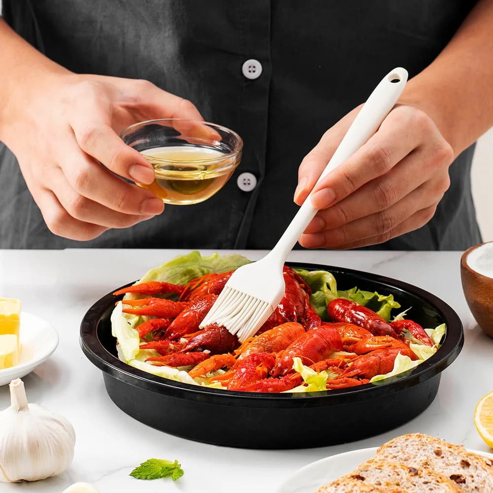 Pessoa usando espátula de silicone branca para pincelar molho em frutos do mar