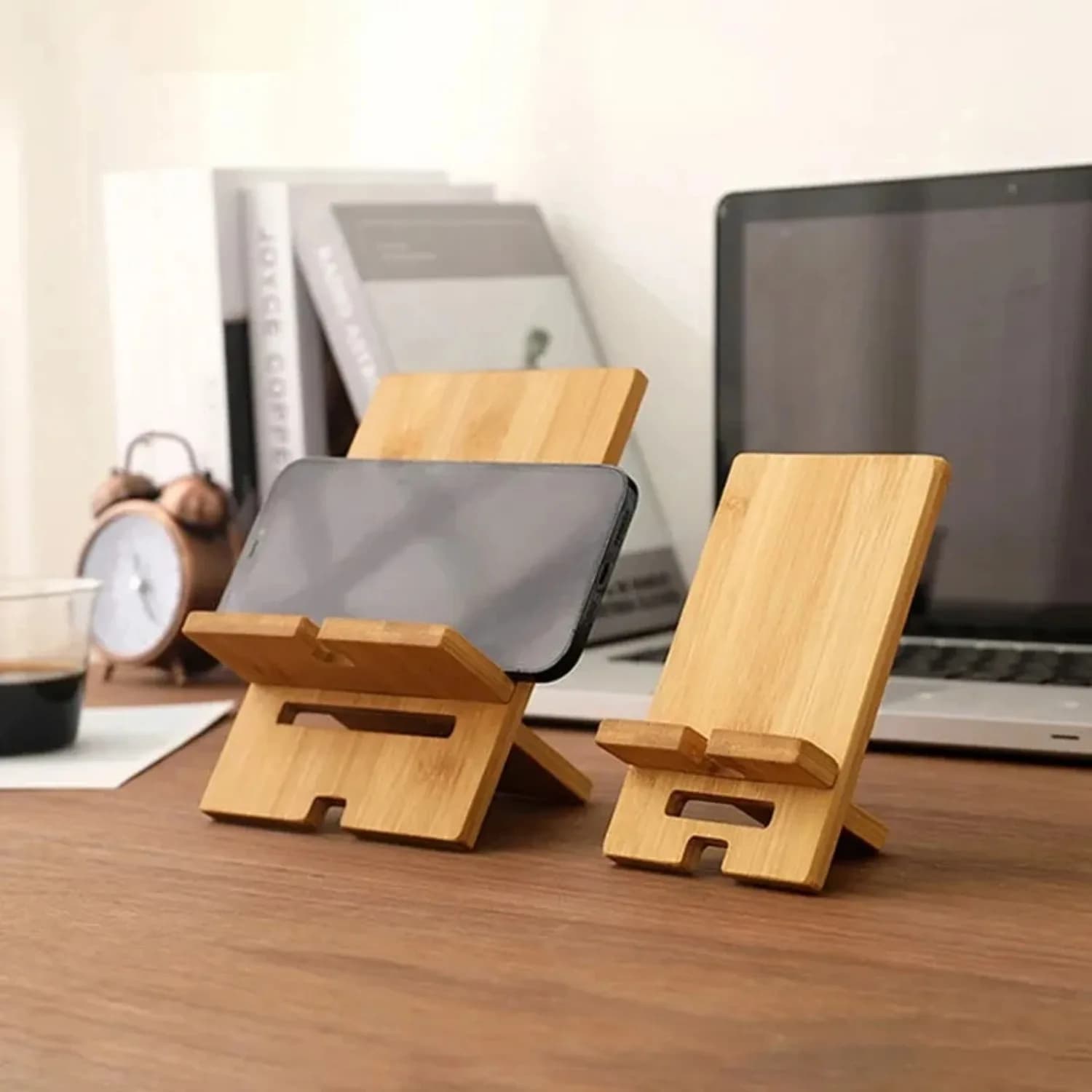 Dois suportes para celular de bambu marrom em mesa de madeira, um com celular na horizontal e outro vazio