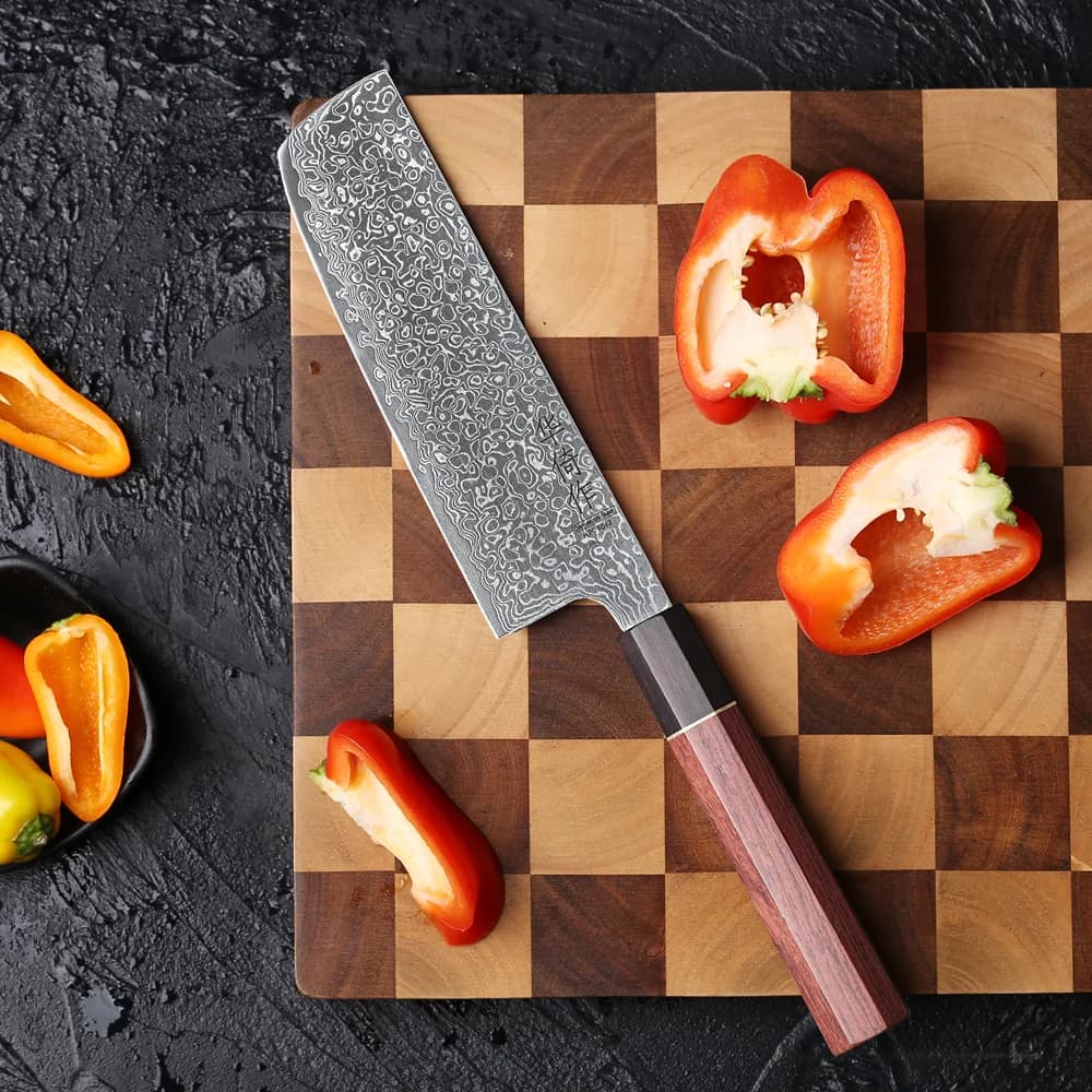 Faca Nakiri de chef 6,5 polegadas em aço damasco com cabo marrom sobre tábua de madeira e pimentões cortados