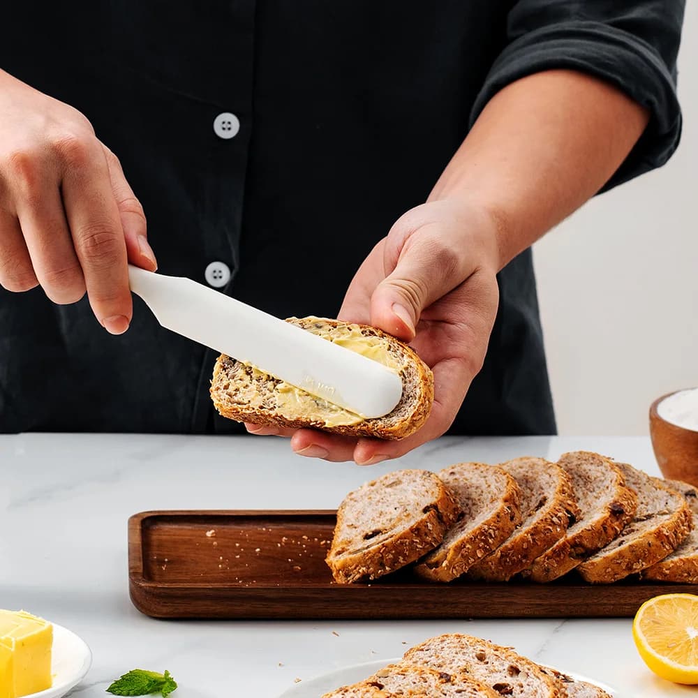 Espátula de silicone branca sendo usada para passar manteiga em fatias de pão integral