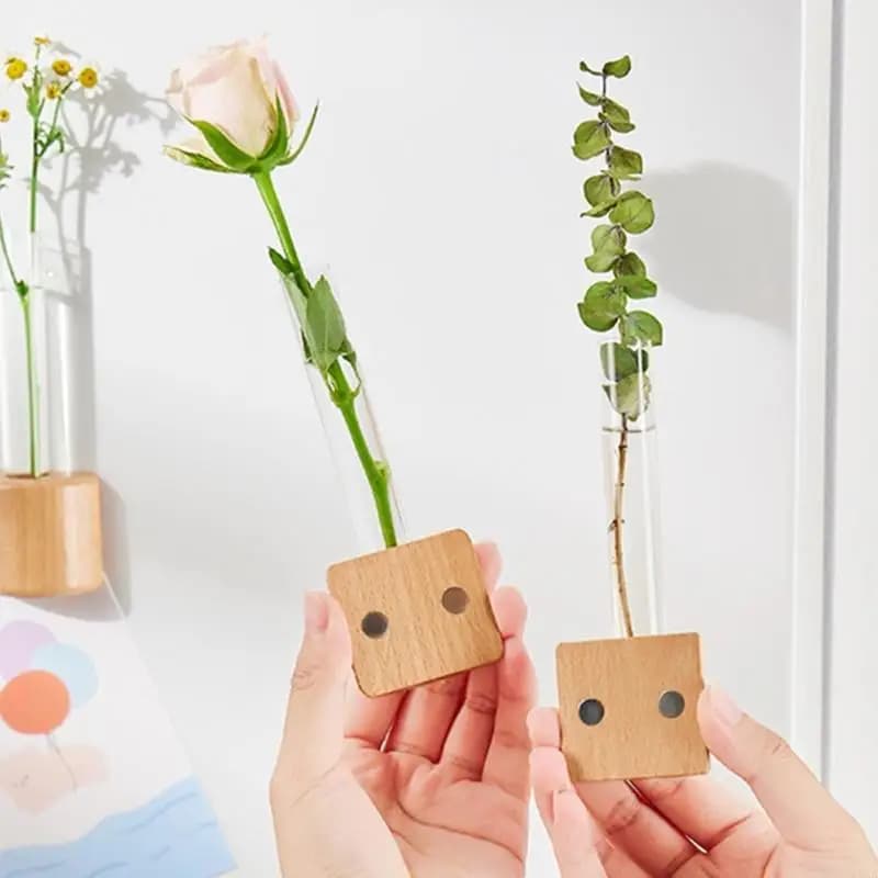 Conjunto 2 vasos Jácotei com tubo de vidro transparente e base de madeira clara segurados por mãos com flores