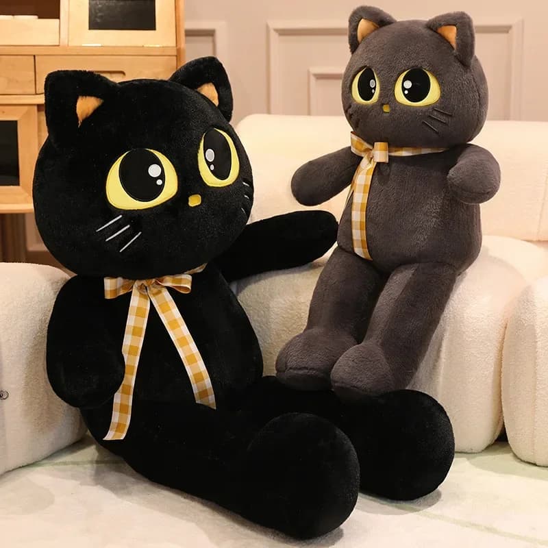 Almofadas de pelúcia em forma de gato preto e cinza com olhos amarelos e gravatas xadrez, sentadas em um sofá branco.
