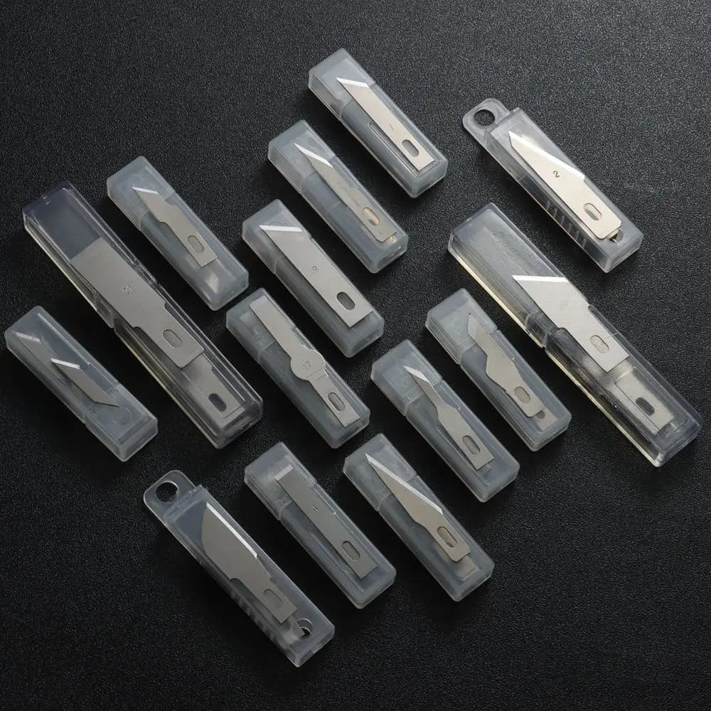 Conjunto de 10 lâminas de facas de escultura em metal, com números de identificação e furos para fixação, sobre fundo preto.