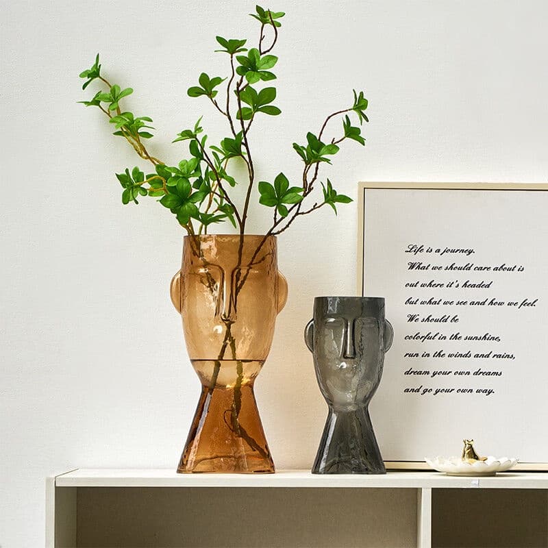 Vasos decorativos em vidro âmbar e cinza com plantas verdes e citação em fundo branco