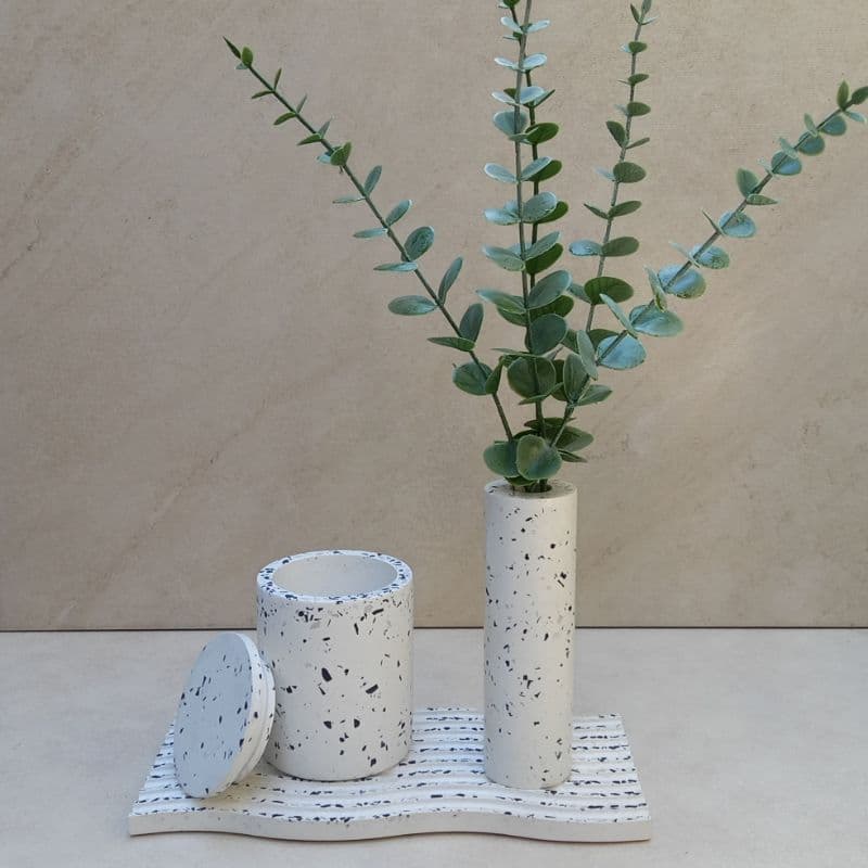 Vaso decorativo cilíndrico branco com manchas pretas contendo planta de eucalipto