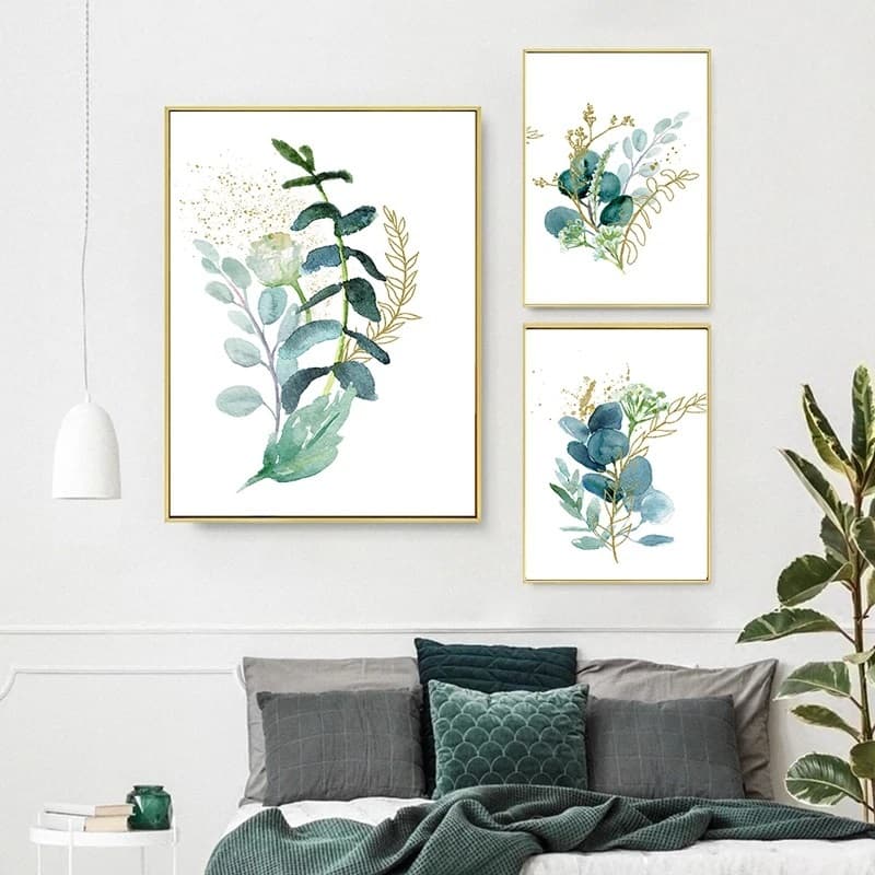 Quadros decorativos com folhas verdes e dourados em uma parede branca, decoração de quarto.