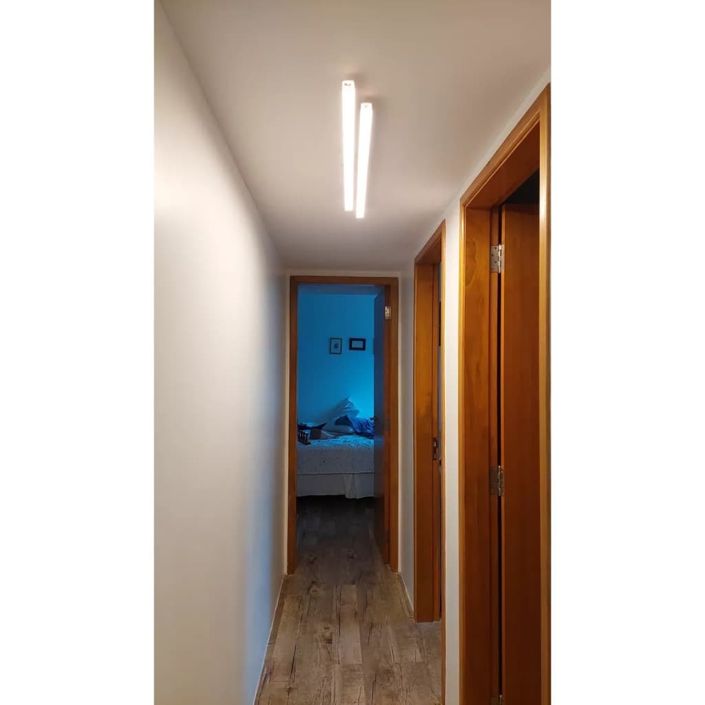 Corredor com iluminação linear LED branca no teto, paredes brancas e piso de madeira.