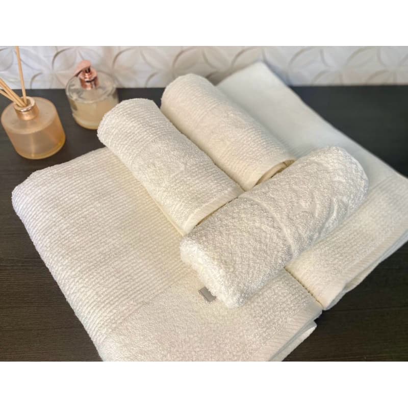 Kit de 5 toalhas MARIA TEREZA brancas, incluindo toalhas de banho, rosto e piso, sobre uma superfície com fundo geométrico.