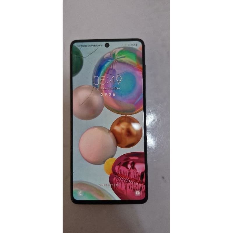 Imagem do smartphone Galaxy A71 com tela trincada, mostrando interface com ícones e hora 05:49.