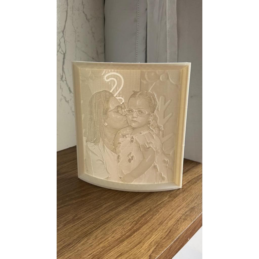 Porta retrato 3D branco com impressão de mãe e criança se beijando, em fundo de madeira