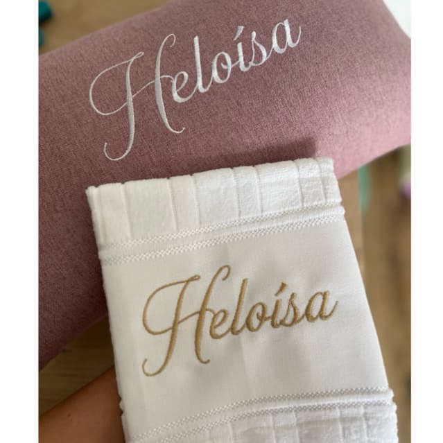 Toalha branca personalizada com nome 'Heloisa' em bordado dourado e almofada marrom com nome 'Heloisa' em bordado prateado
