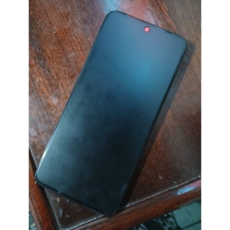 Verso do smartphone Xiaomi Redmi note 12 em preto, sobre uma mesa de madeira.