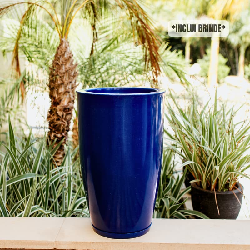 Vaso azul grande para plantas com acabamento marmorizado, em um ambiente externo com plantas verdes ao fundo.